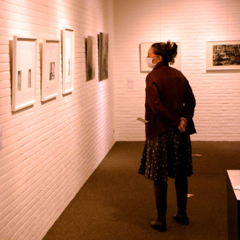 Une visiteuse, debout face à des oeuvres accrochées au mur
